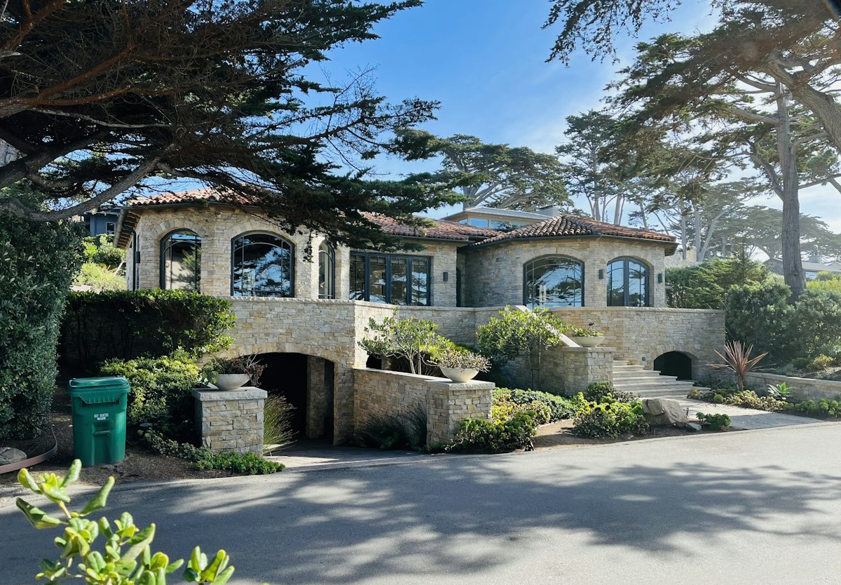 A stone house with arched windows behind cypress trees